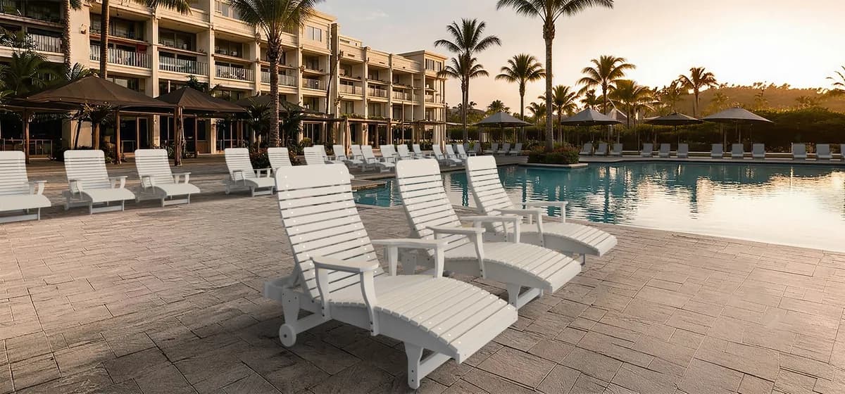 Rows of white Wildridge poly chaise lounges lining a resort pool deck at sunset, framed by palm trees and guest room balconies