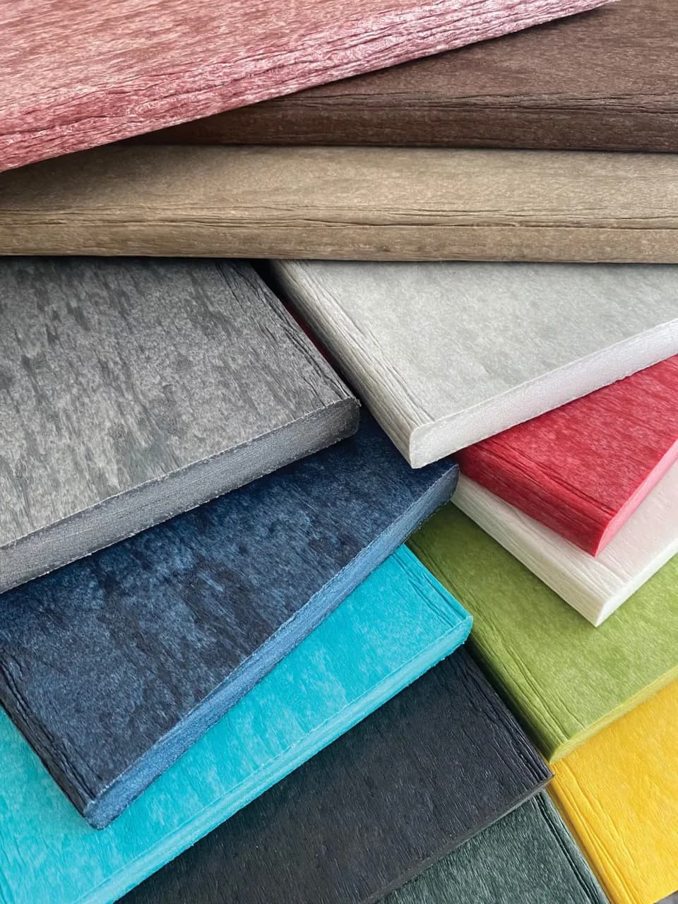 Close-up of stacked Wildridge poly lumber sample swatches in cedar, weathered wood, gray, patriot blue, aruba blue, red, white, lime green, and yellow
