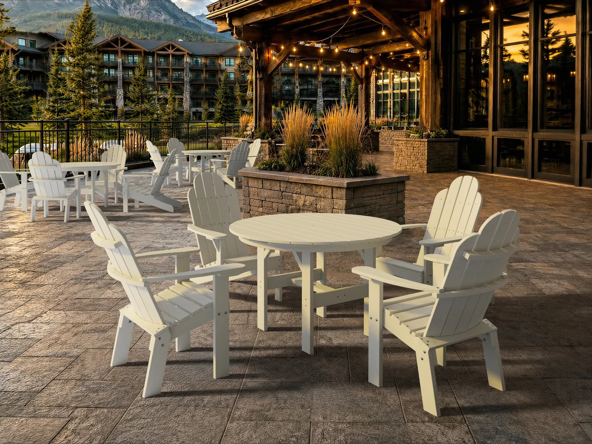 White Wildridge poly Adirondack dining chairs and round tables filling a mountain lodge terrace under a timber pergola strung with lights